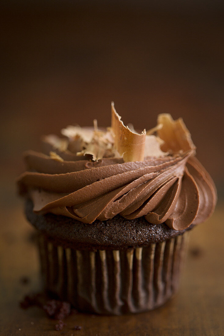 A chocolate cupcake with a cream topping and chocolate shavings