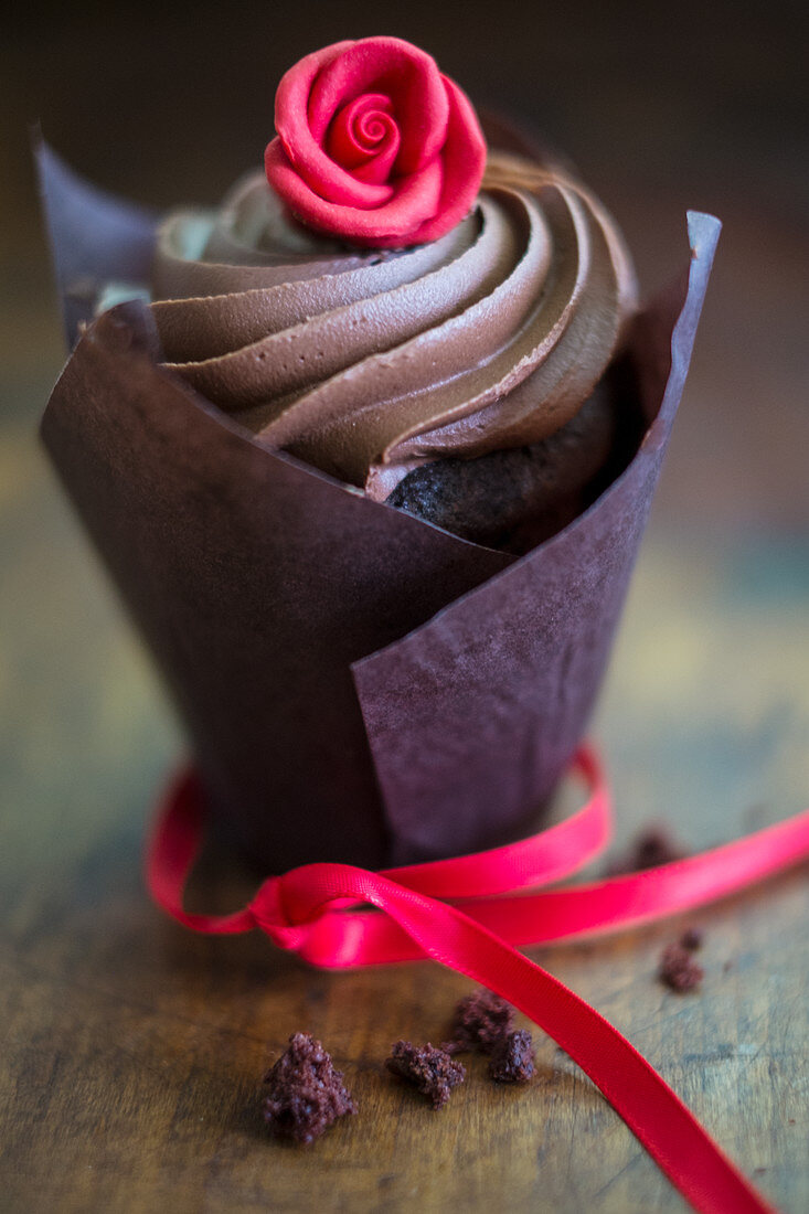 A chocolate cupcake with a cream topping and a marzipan rose