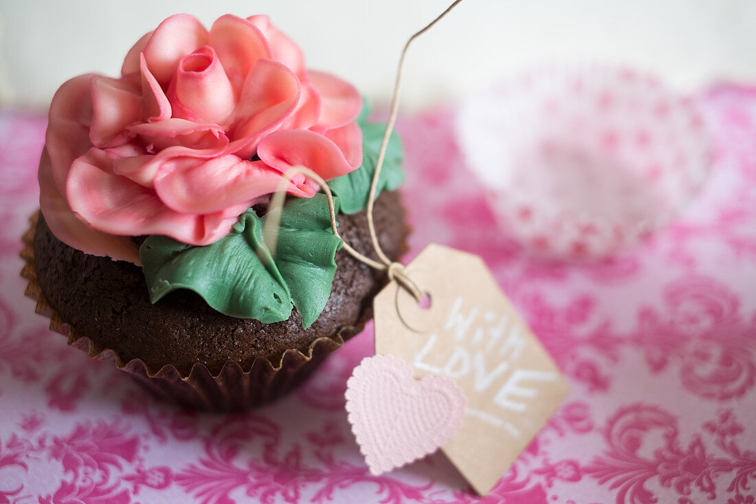 A cupcake decorated with a large sugar rose and a gift tag