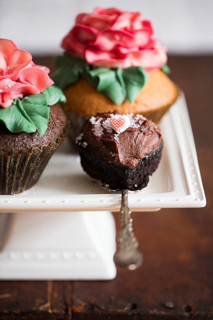 Cupcakes decorated with large sugar roses on a cake stand and a chocolate cupcake
