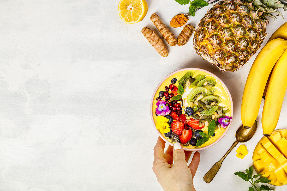 Mango banana pineapple turmeric breakfast superfoods smoothie bowl topped with fruits, berries and seeds