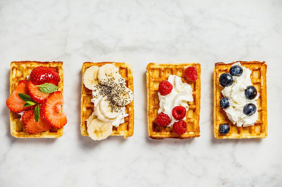 Traditional belgian waffles with whipped cream and fresh fruits and berries on white marble background