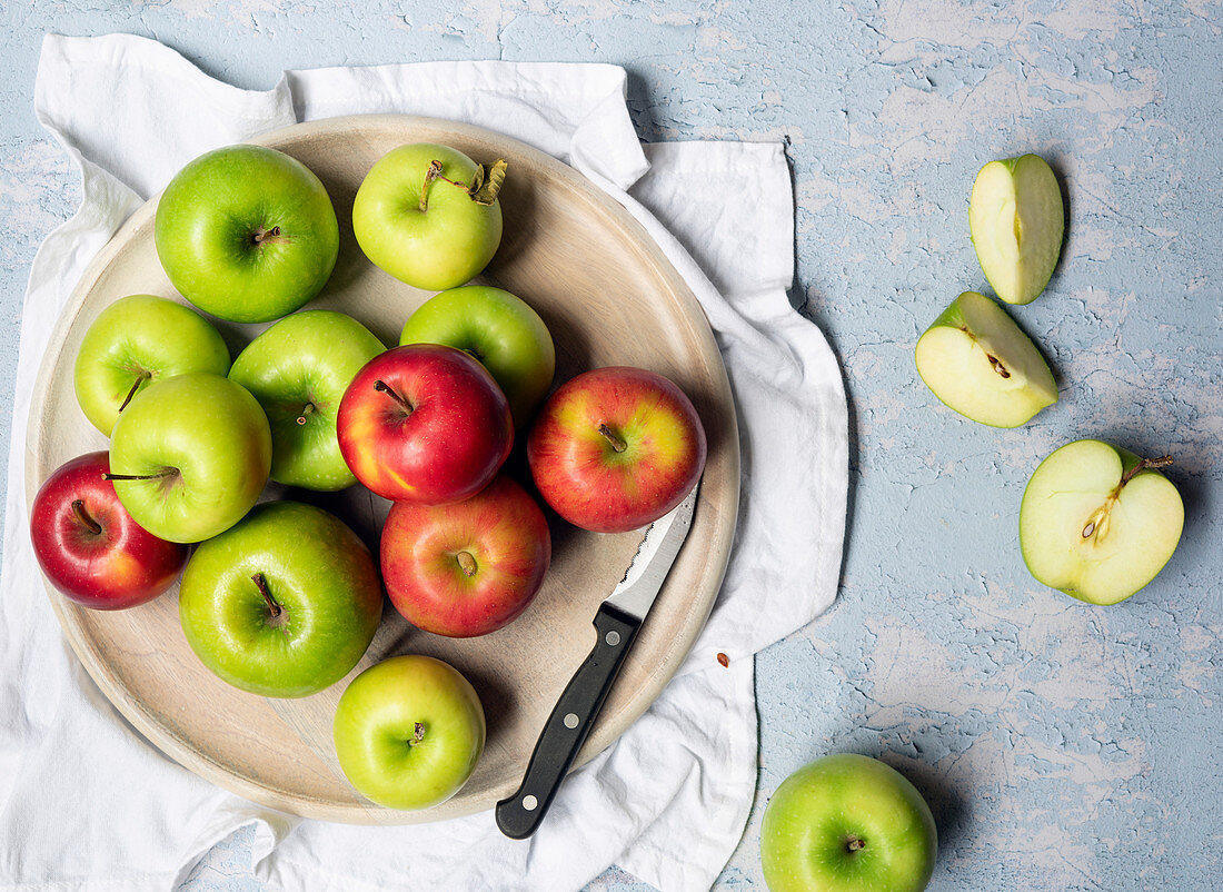 Green cooking apples and red eating apples with a knife on a round wooden board