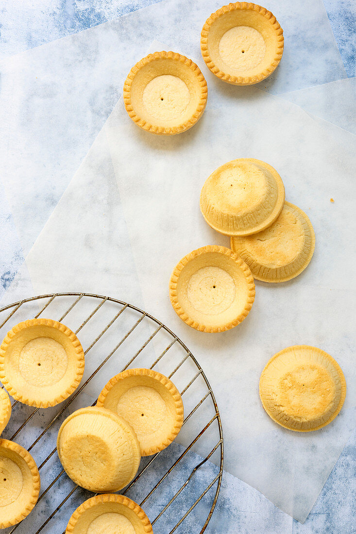 Small baked pastry tartlet cases cooling on a wire rack and baking paper
