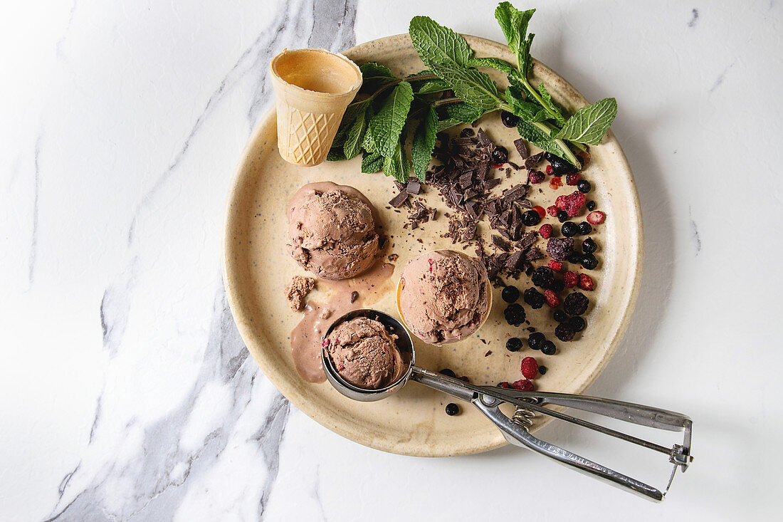 Himbeer-Schokoladeneis, Eistüte, Eiskugelformer, Minze, Beeren und Schokolade auf Teller