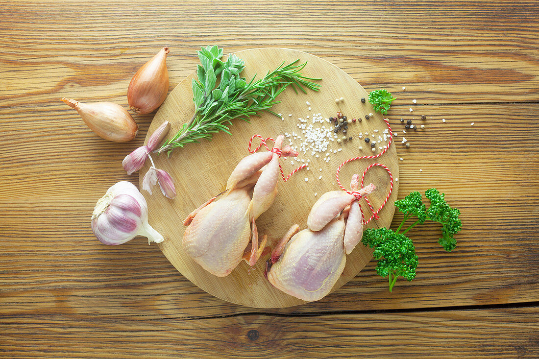 Raw corn-fed quail's with ingredients on a wooden surface