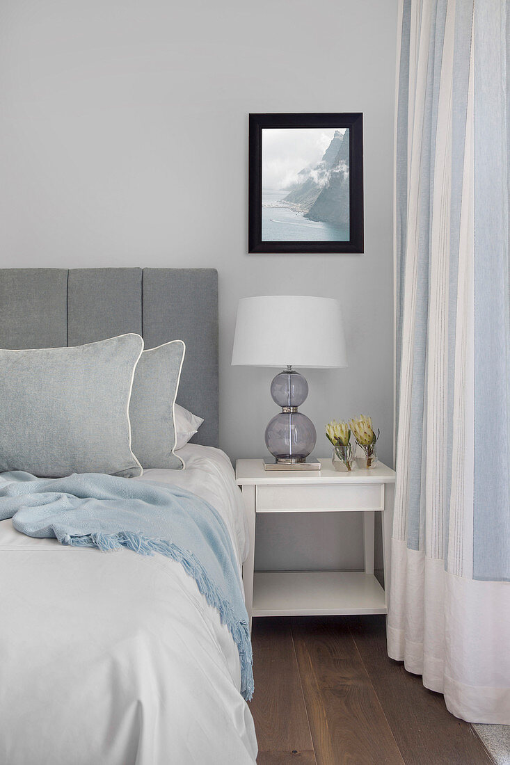 Bed with grey headboard and white bedside table in bedroom