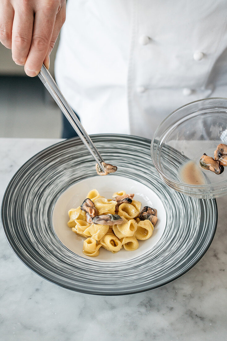 Koch beim Anrichten von Tortellini mit Krustentier-Bisque, Miesmuscheln und Sauerrahm