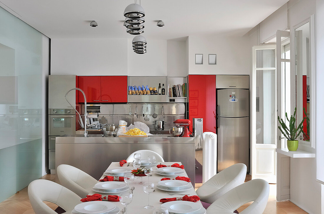 Set dining table in front of open-plan kitchen with red accents