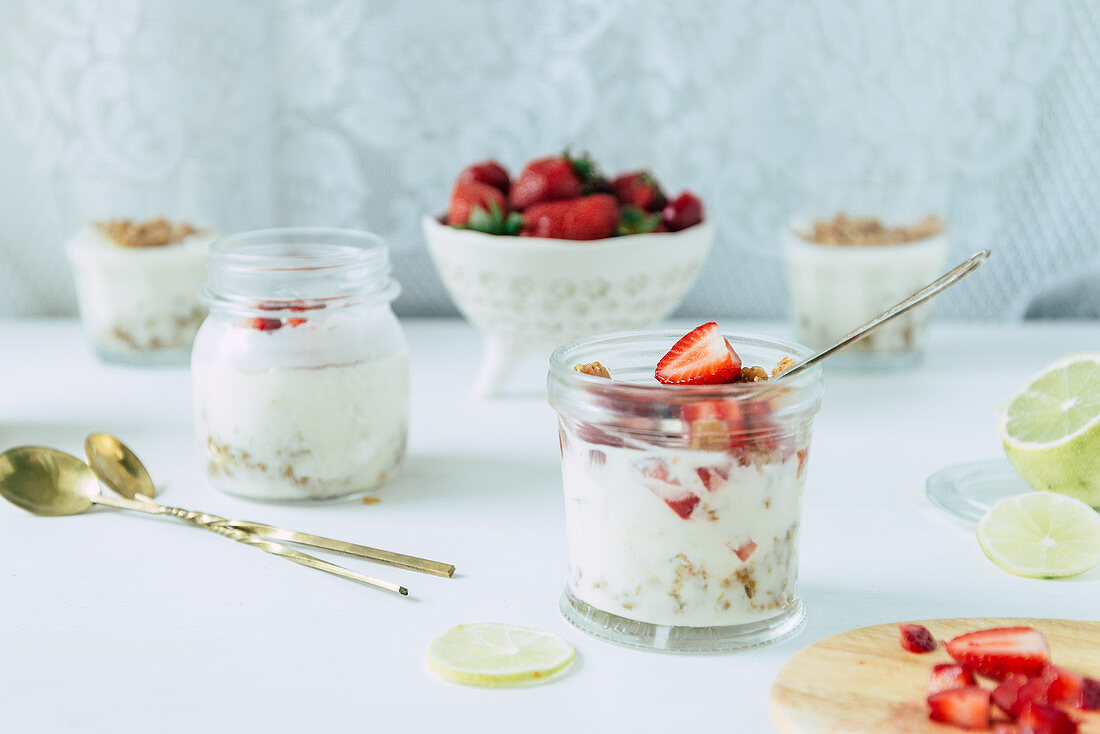 Lime and strawberry posset with streusel in glass jars on a white background