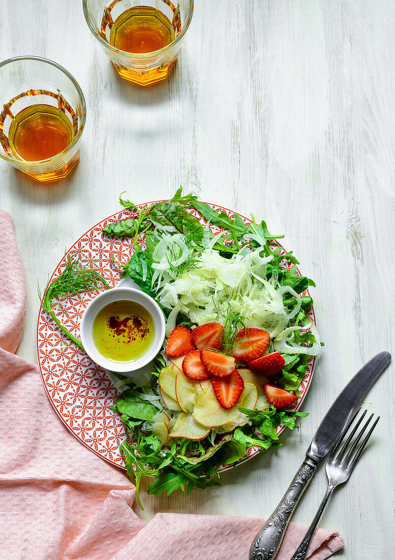 Top down view of a plate of fresh fennel and red apple salad garnished with fresh strawberries