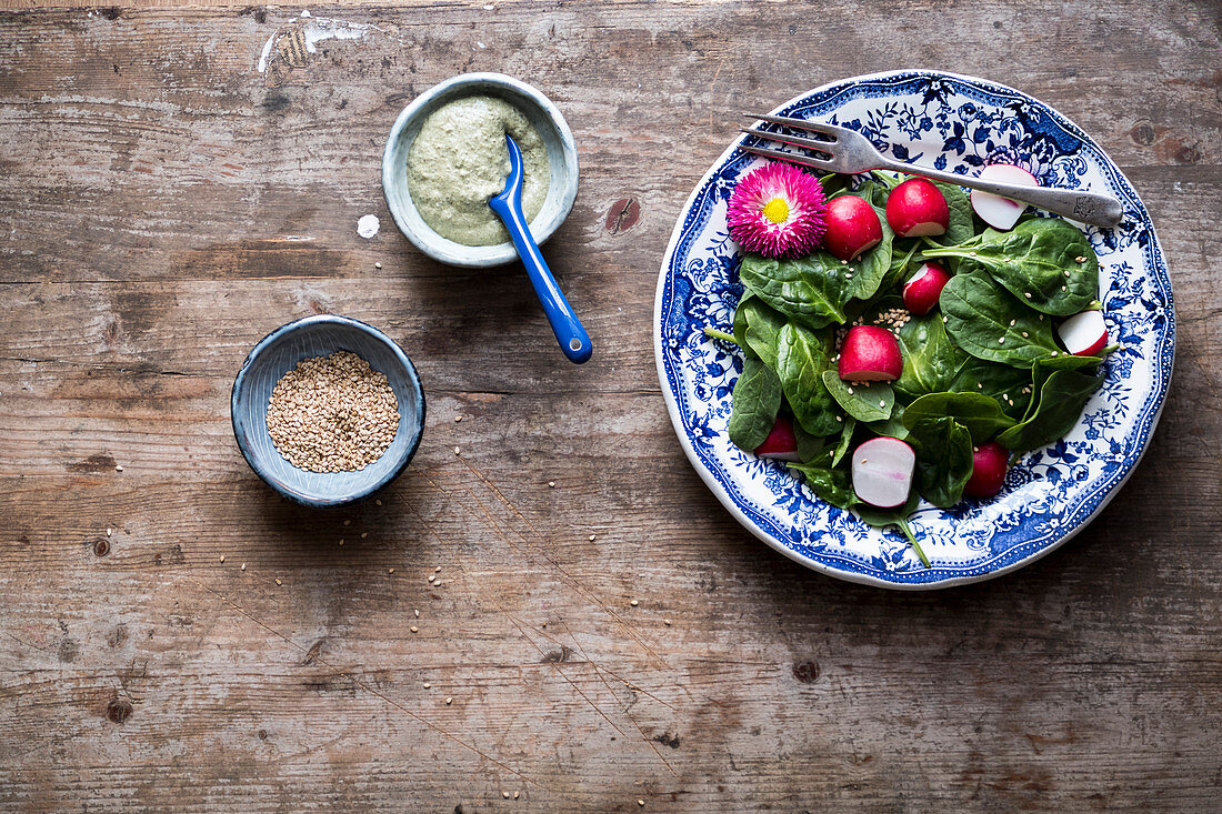 Salad with radish and spinach with a dressing and sesame seeds on a wooden table and a blue bowl