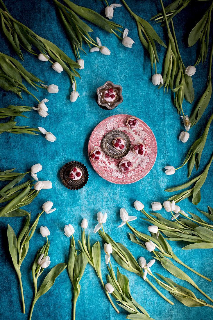 Rosa Törtchen mit Himbeeren, umgeben von weissen Tulpen