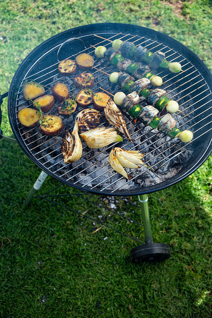 Fish skewers, potatoes and fennel on a grill