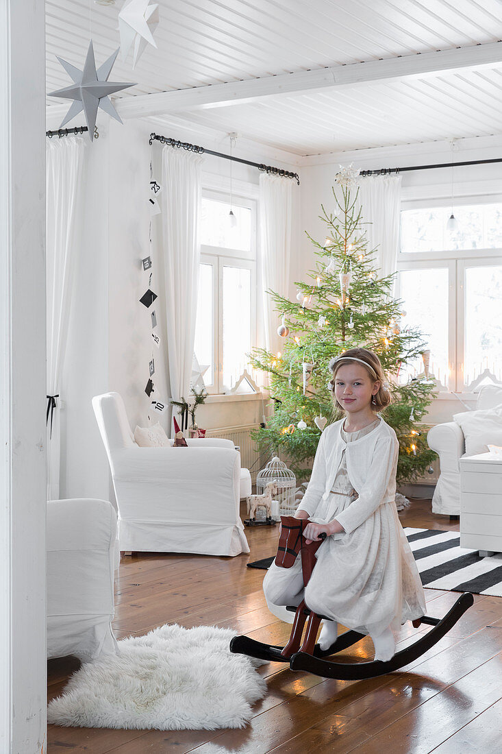 Girl on rocking horse in front of Christmas tree in living room