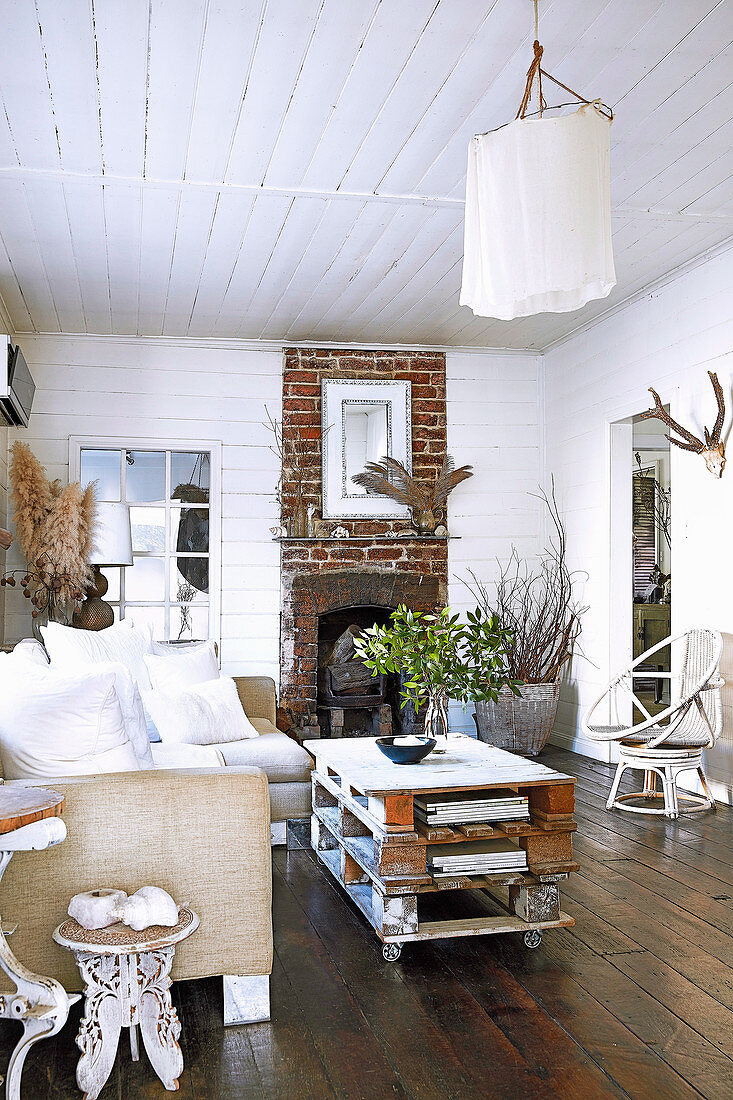 Rustikaler Palettentisch, Sofa und Kamin im Wohnzimmer mit Dielenboden