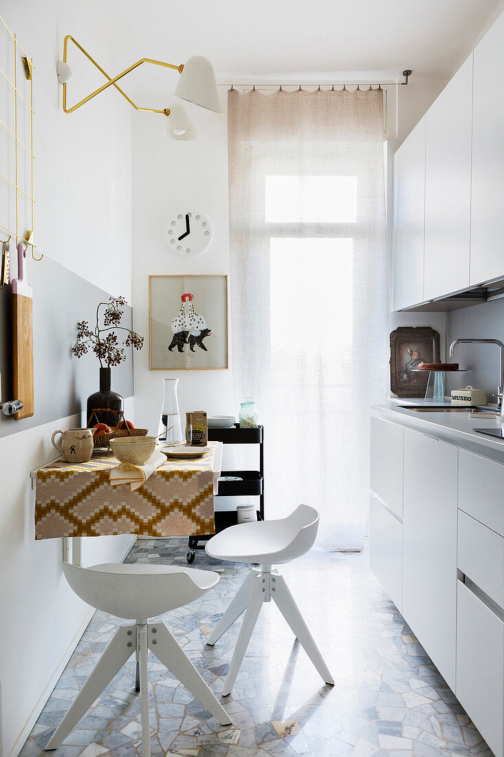 White kitchen counter, wall-mounted table and bar stools in narrow kitchen