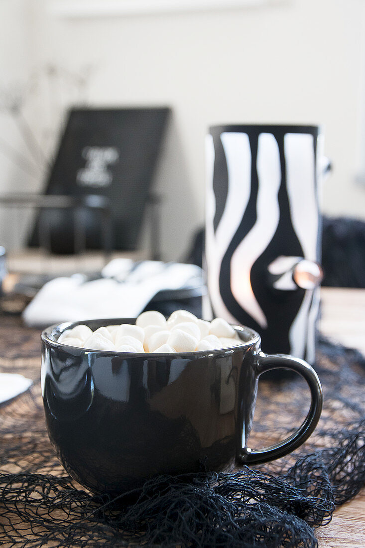 Heisses Getränk mit Marshmallows in schwarzer Tasse, im Hintergrund DIY-Windlicht