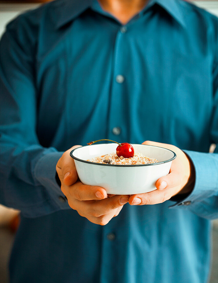 Hands holding a bowl of muesli and cherries
