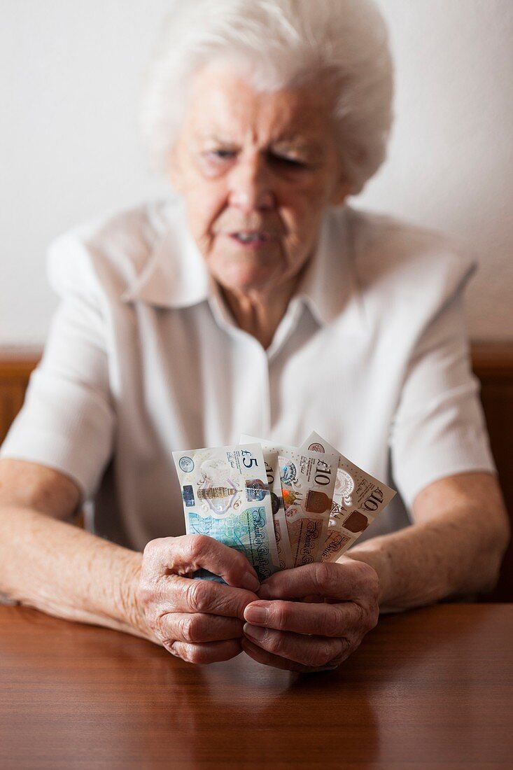 Worried elderly woman counting British banknotes
