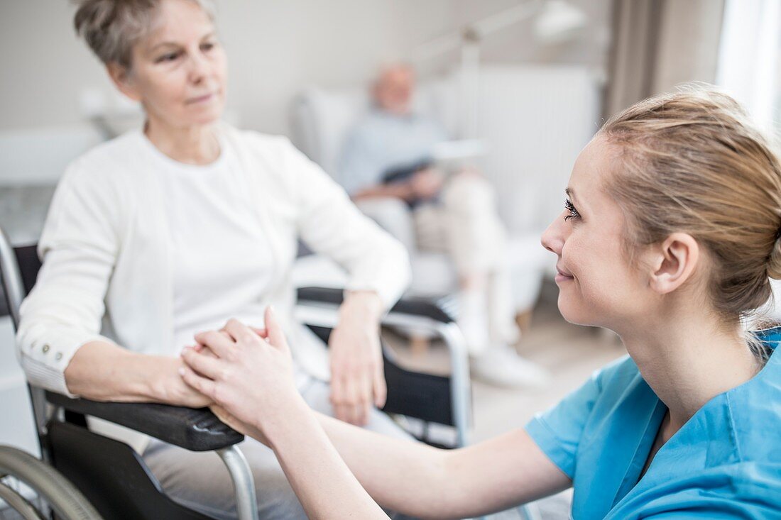 Carer reassuring senior woman in wheelchair