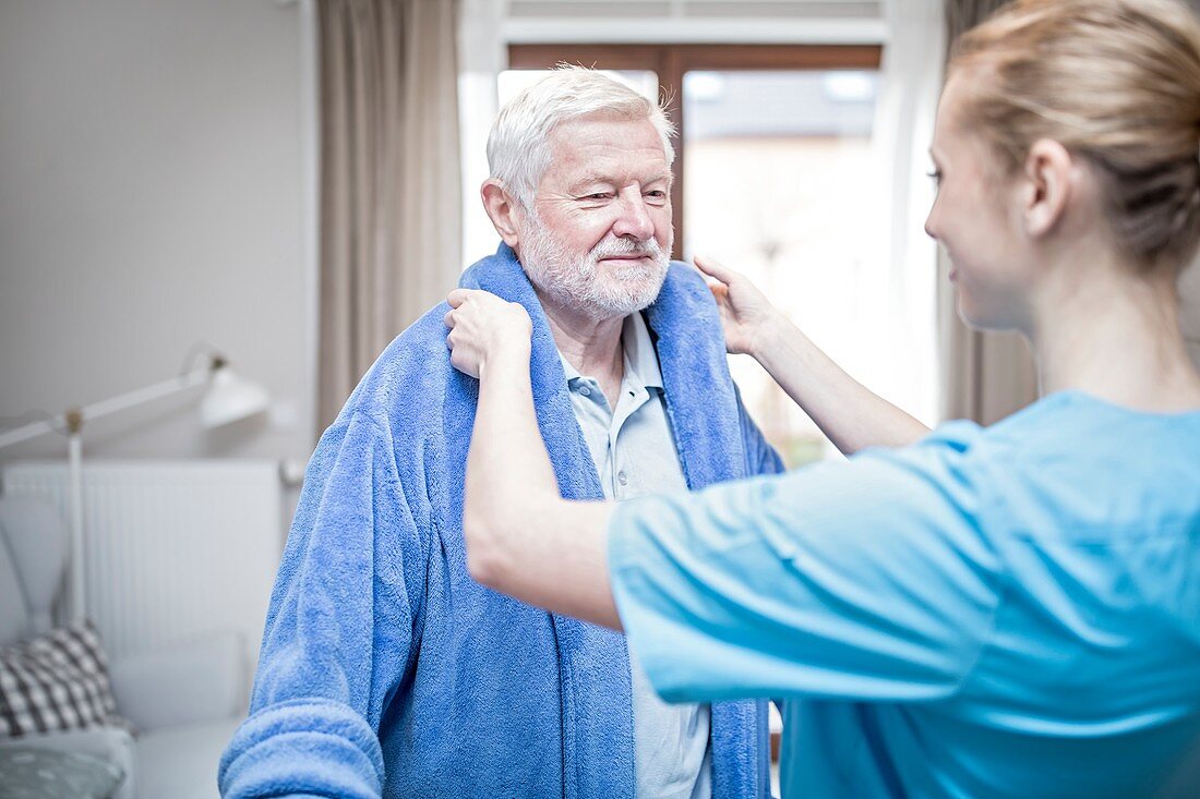 Carer helping man put on dressing gown