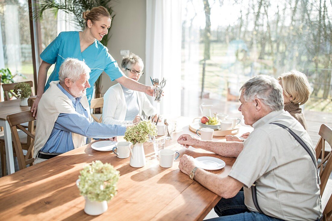 Carer serving seniors at dinner table