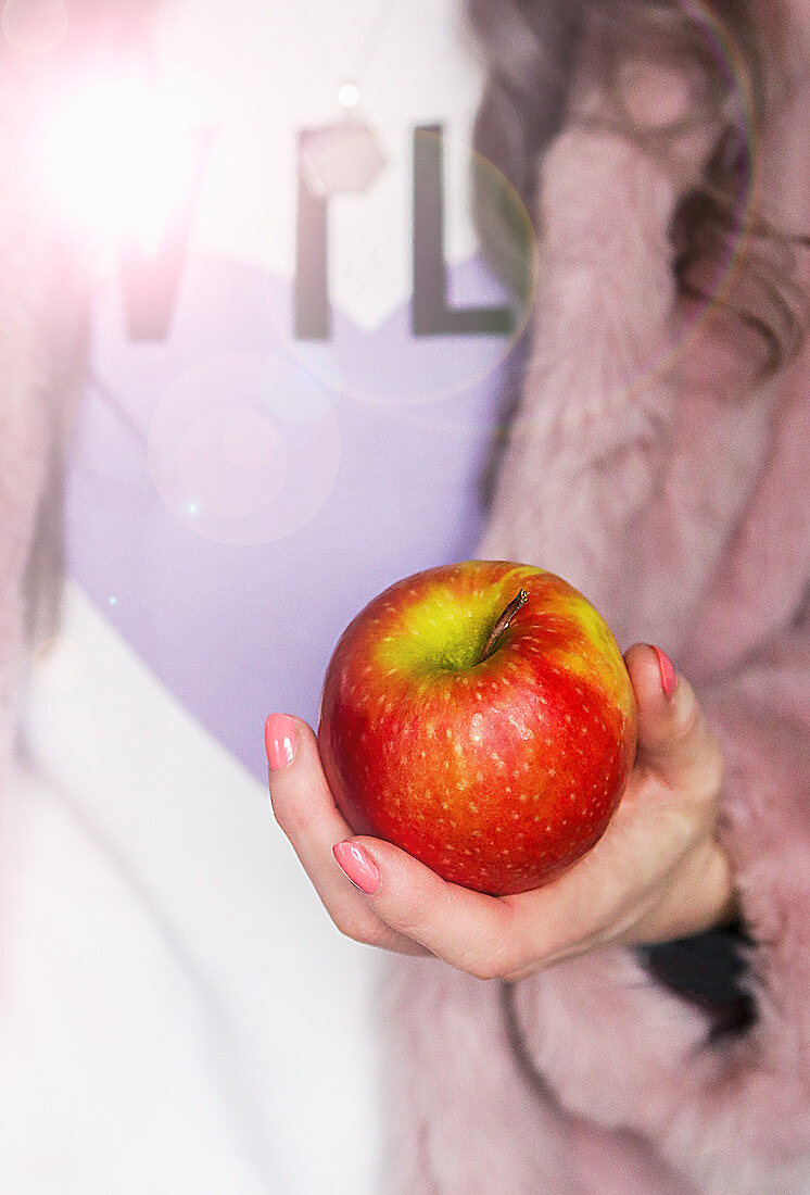 Red and green apple being held in a female hand