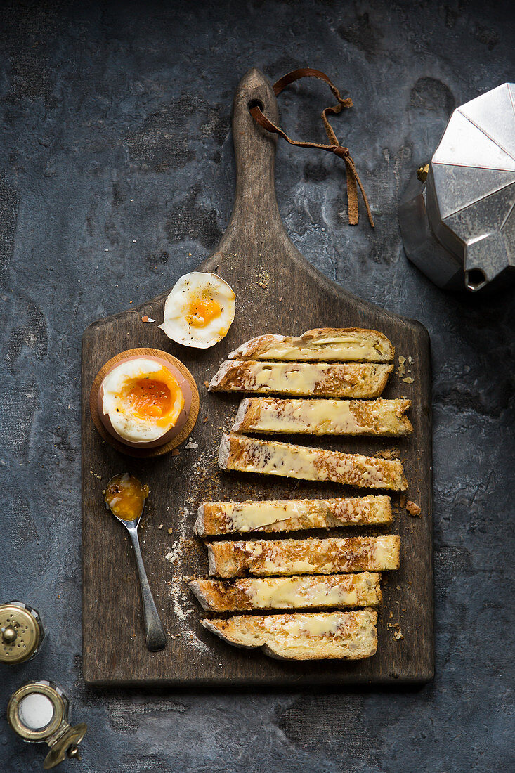 Soft boiled dippy egg with toasted soldiers on a wooden board and moody trendy setting