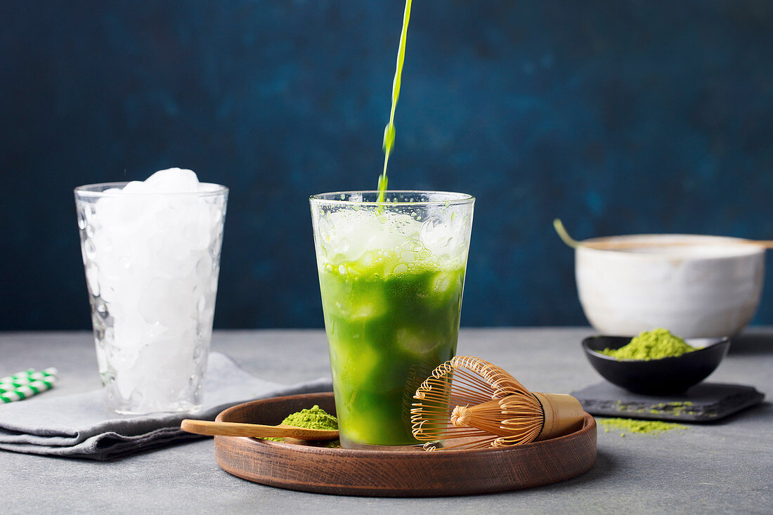 Matcha, green tea ice tea pouring in tall glass on wooden plate