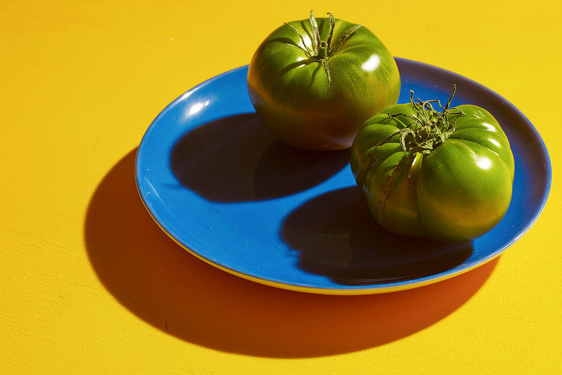 Two green tomatoes on a blue plate