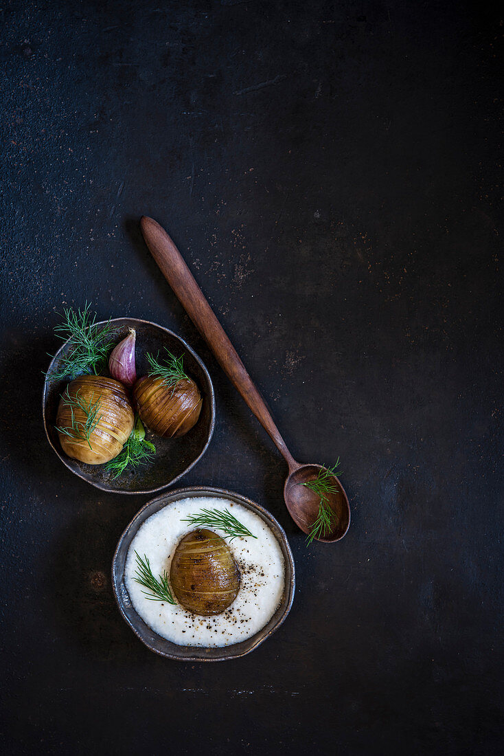 Hasselback potatoes with yoghurt and fresh dill on dark background, flat lay