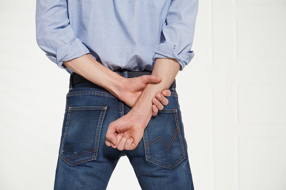 A man holding onto his wrist with a fist behind his back