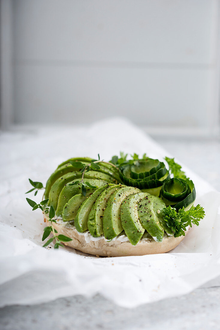 A sesame bagel with almond cheese, avocado, cucumber and fresh herbs (vegan)