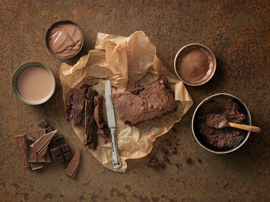 Chocolate cake on baking paper, cocoa powder, chocolate, and chocolate buttercream