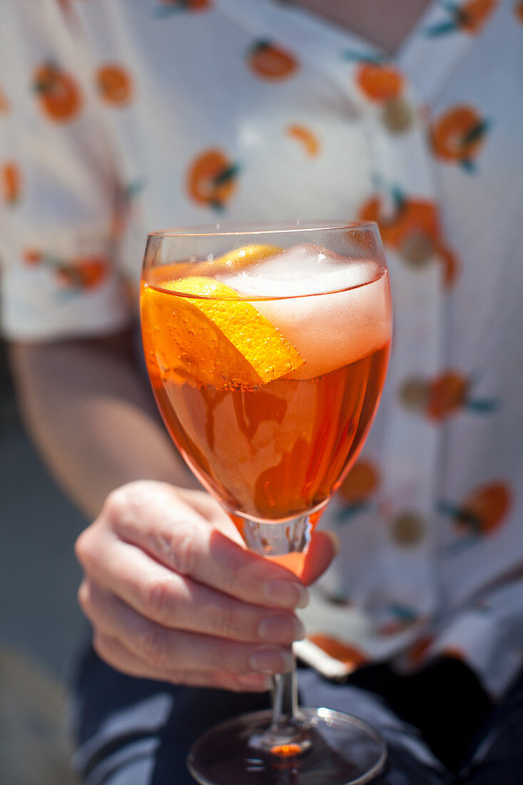 A woman holding a glass of Aperol Spritz with a citrus slice