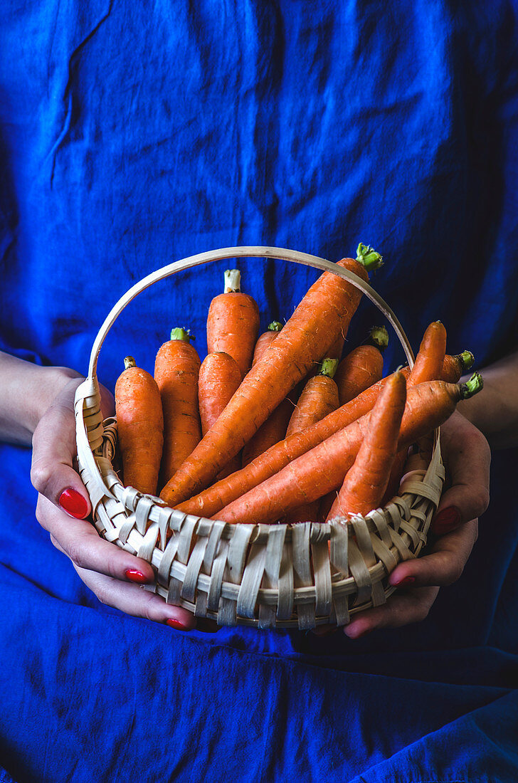 A woman holding a basket of fresh carrots