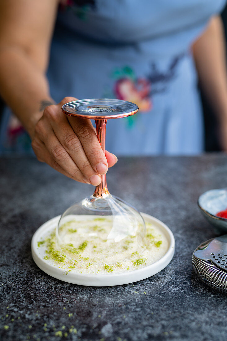 Rand eines Cocktailglases mit Zucker und Limettenzesten verzieren