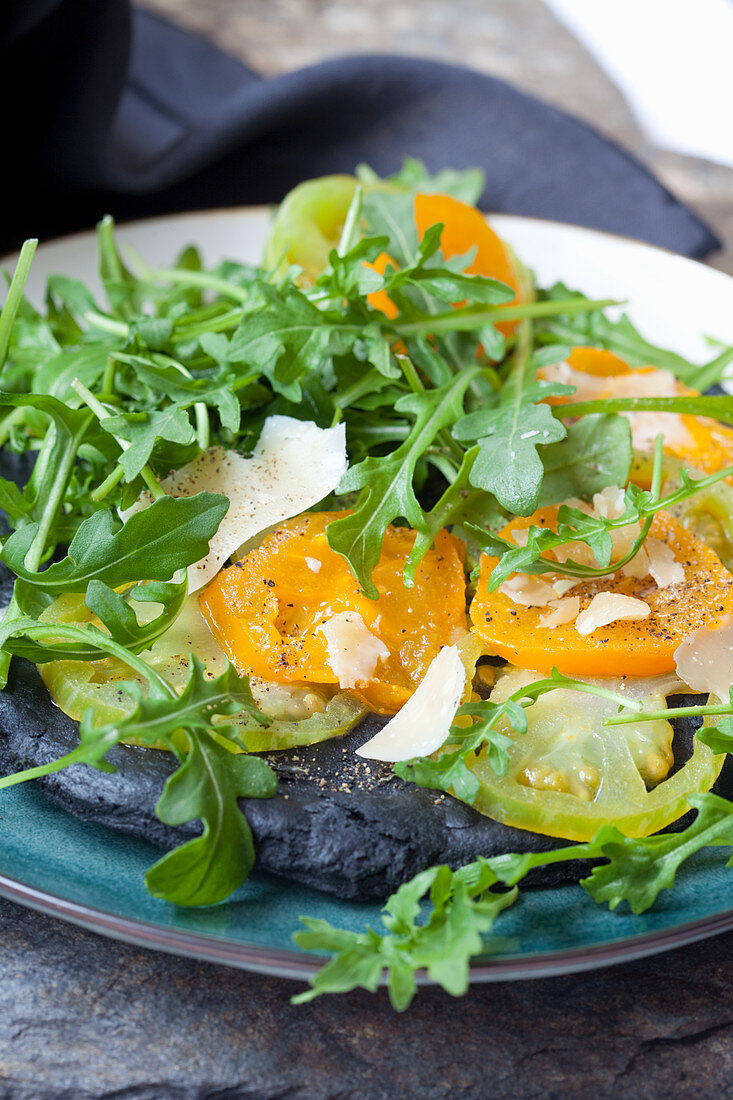 Black pizza with activated charcoal, green and yellow tomatoes, Parmesan cheese and rocket