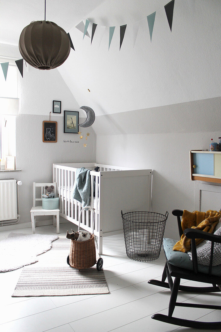White cot and rocking chair in nursery with white wooden floor