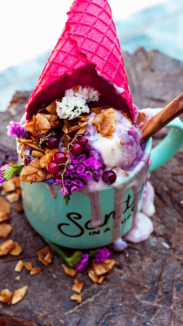 Waldbeereneis serviert in Tasse mit pinkfarbener Waffeltüte und Kokosflocken