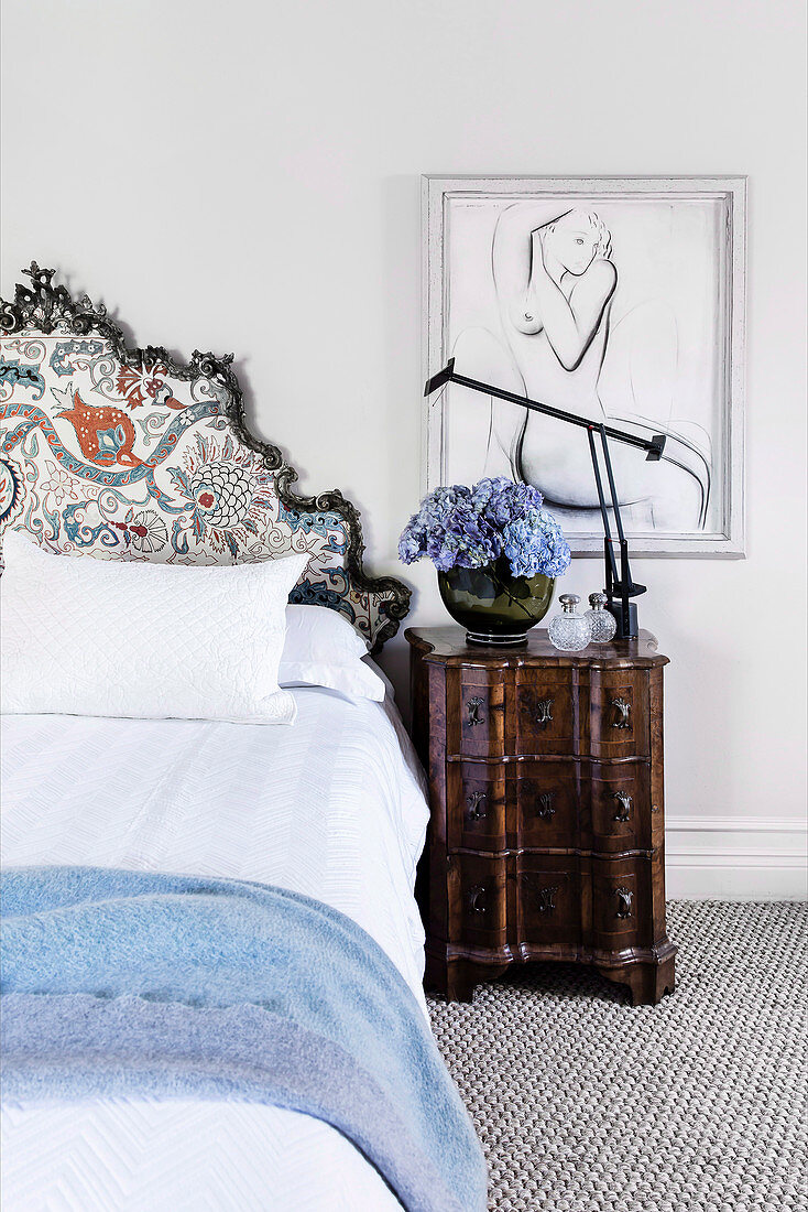 Double bed with handcrafted bed head next to antique bedside tables