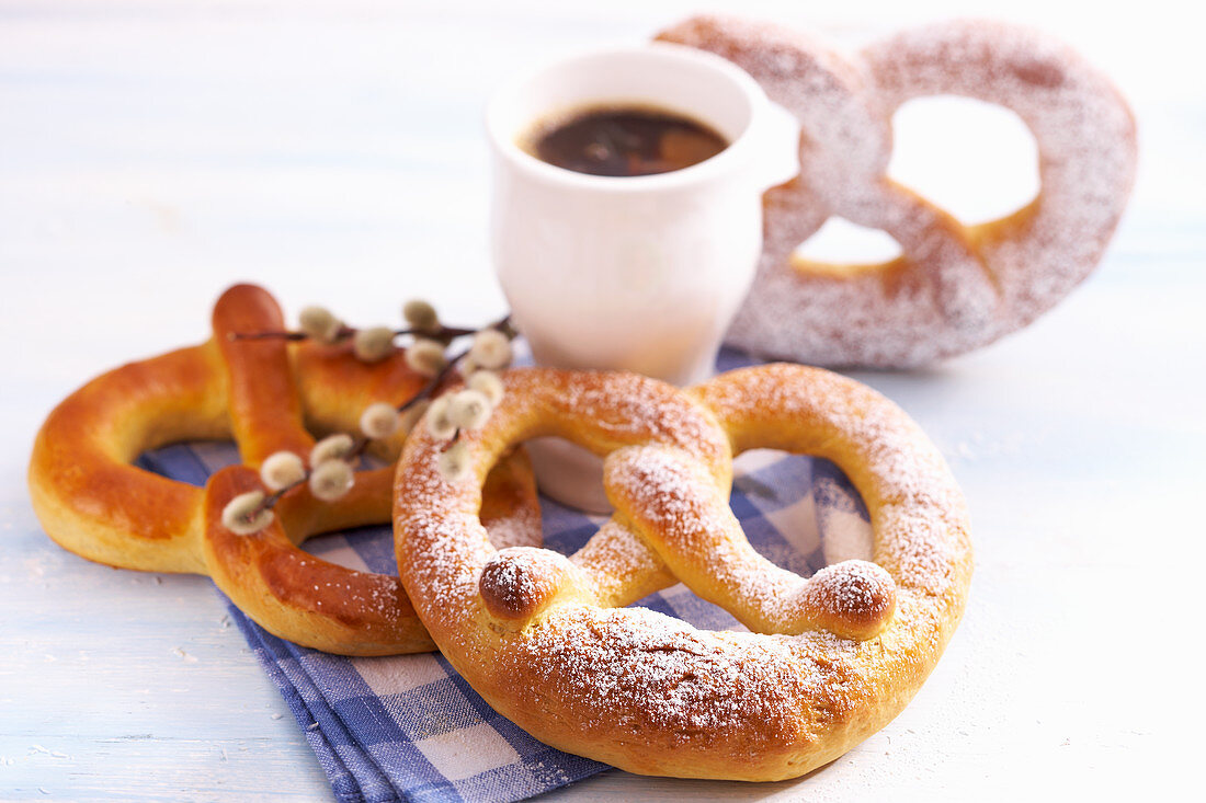 Süsse Brezen aus Hefeteig zu Ostern auf Serviette mit Tasse Kaffee und Palmkätzchen