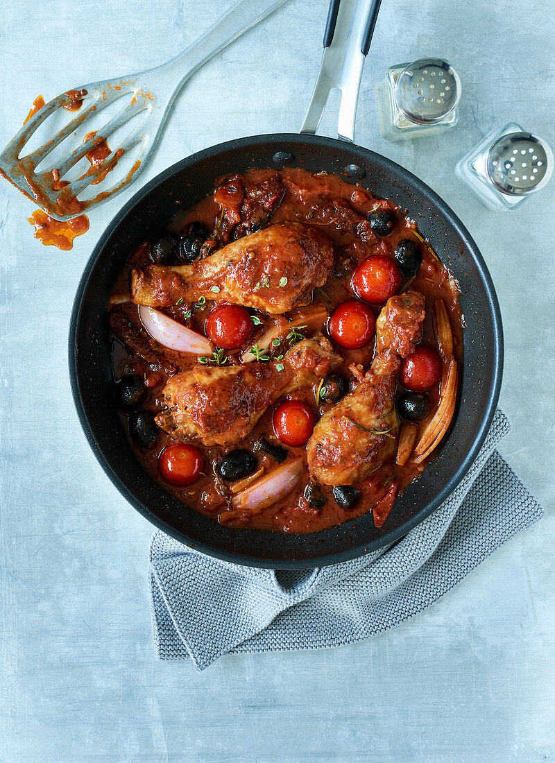 Mediterrane Hähnchenkeulen mit Zutaten und Sauce in Pfanne mit Salz und Pfefferstreuer