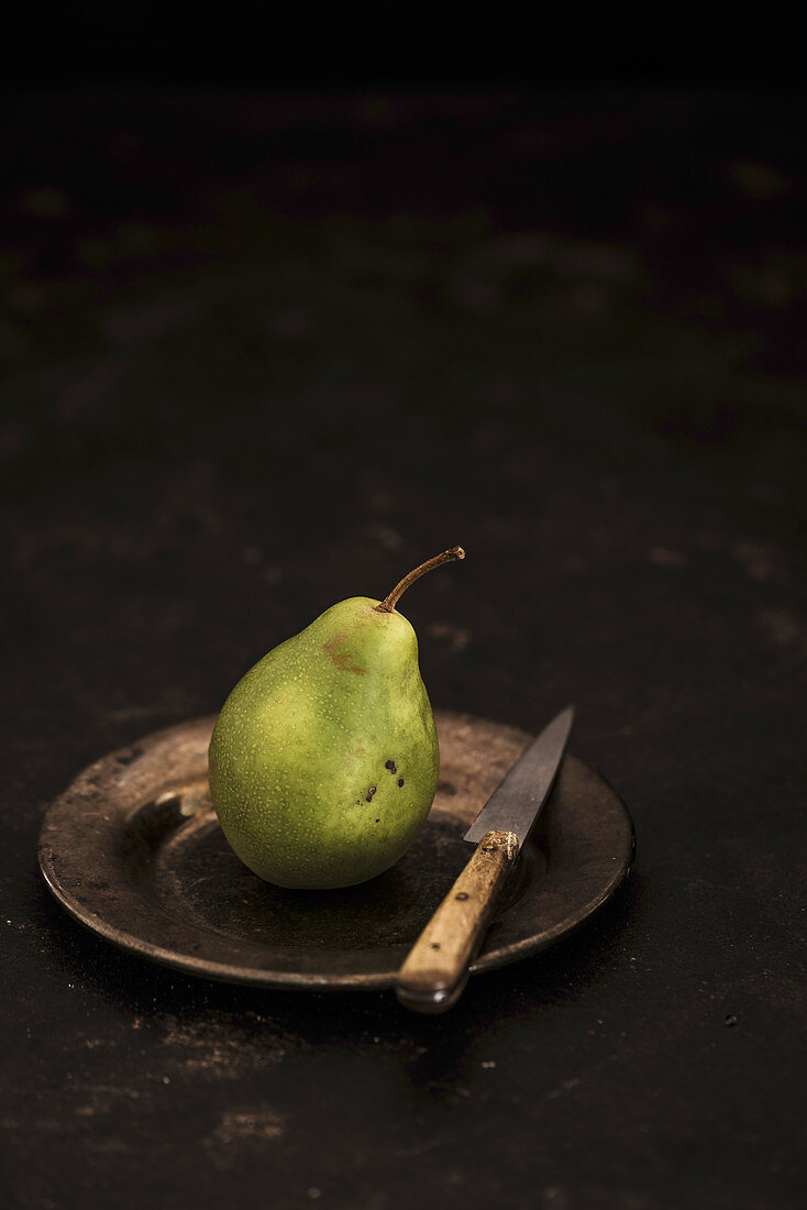 A pear on a tin plate with a knife