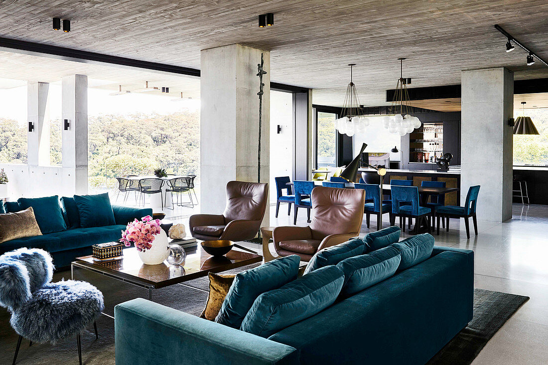Various seating furniture around coffee table, in the background dining area in open living room with exposed concrete ceiling