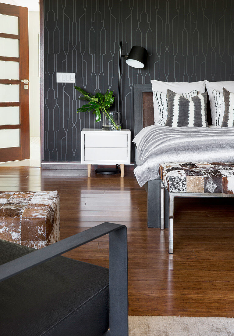 Double bed and white bedside cabinet in bedroom with black wallpaper