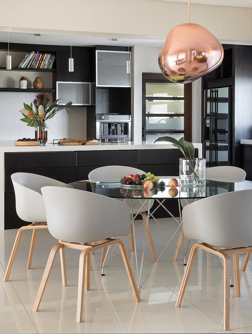 Round glass table and designer chairs in dining area in front of kitchen island