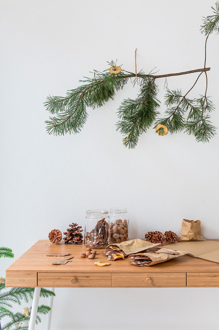 Pine branch decorated with apple rings above biscuits and pine cones on table