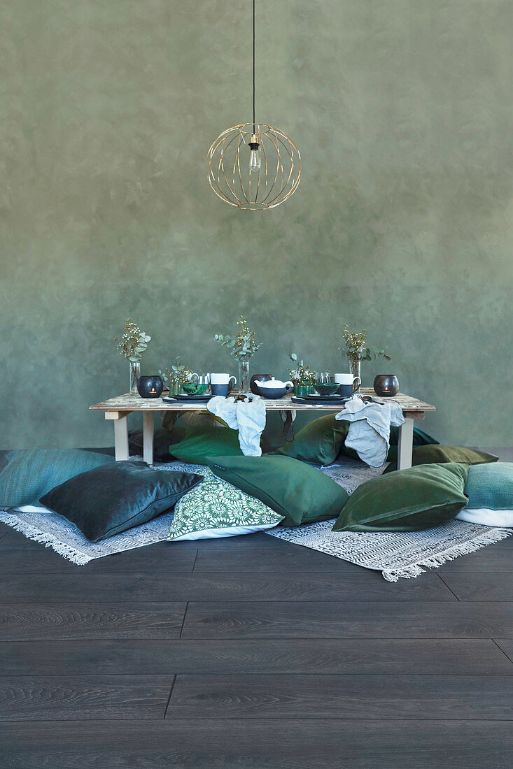 Grüne Kissen am Boden um einen niedrigen, gedeckten Tisch